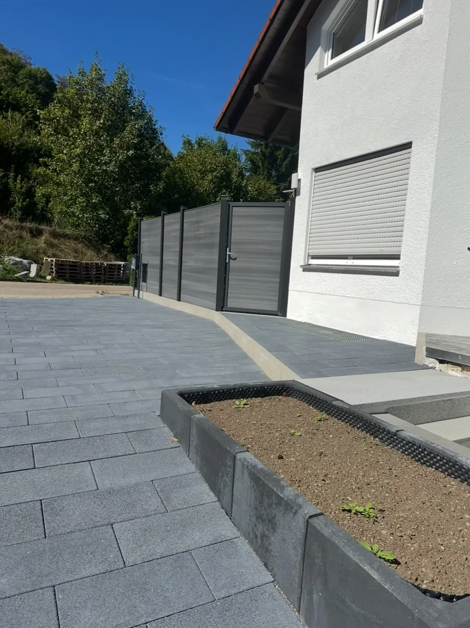 Anthrazitfarbener Sichtschutzzaun mit Gartentür neben einer Pflasterfläche und einem neuen Hochbeet