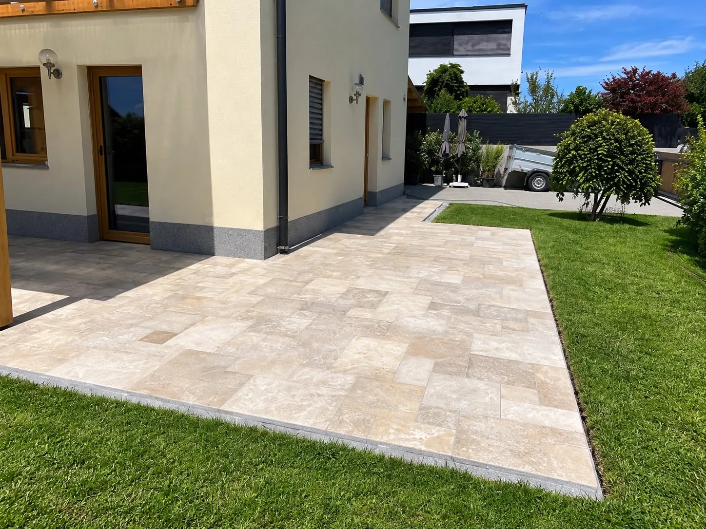Terrasse aus beigen Natursteinplatten im Römischen Verband mit sauberer Kante zum Rasen