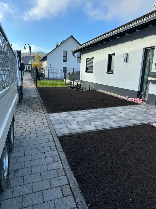 Vorgarten mit frisch eingebautem Oberboden und neuem Plattenweg zur Haustür