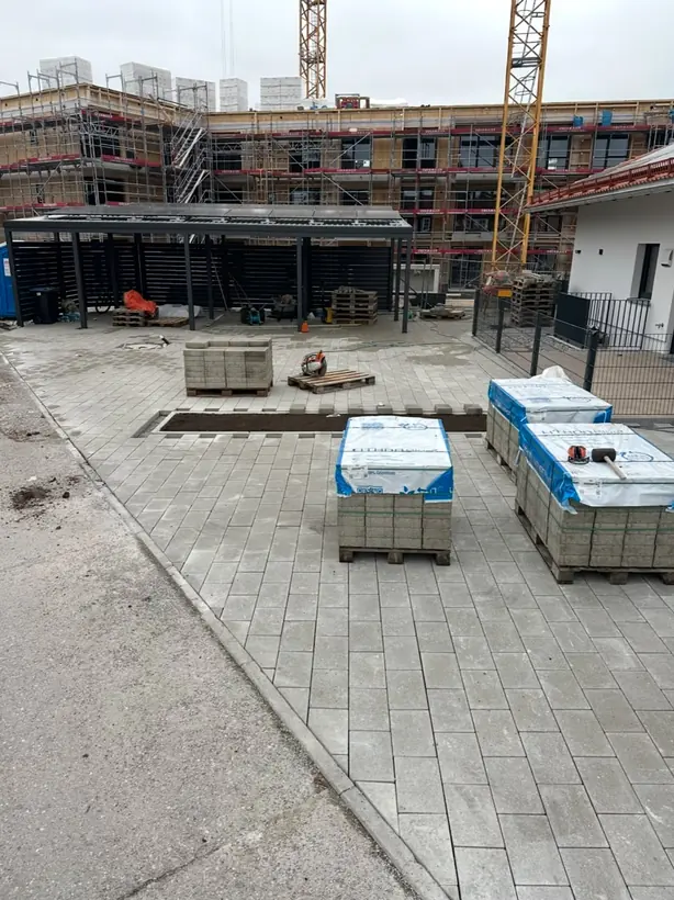 Neue Pflasterfläche an einer Wohnanlage im Bau, mit Steinpaletten und Carport